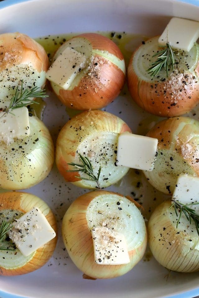 roasting onions in a pan topped with butter and rosemary sprigs