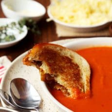 A grilled cheese sandwich dipped in tomato soup bowl.