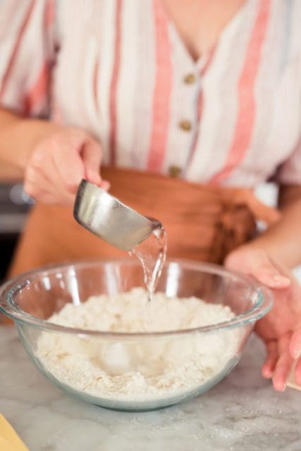 Adding cold water to pie crust ingredients.