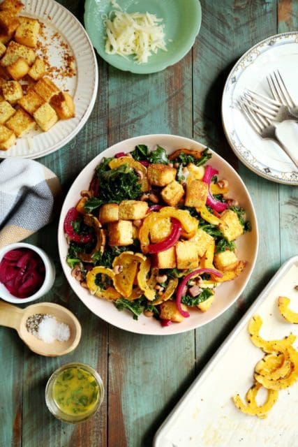 Kale salad in a bowl with roasted squash, pickled red onions, and cornbread croutons