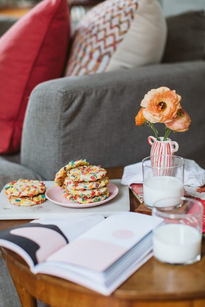 A stack of baked Fruity Pebble Cookies on a pink plate with milk.