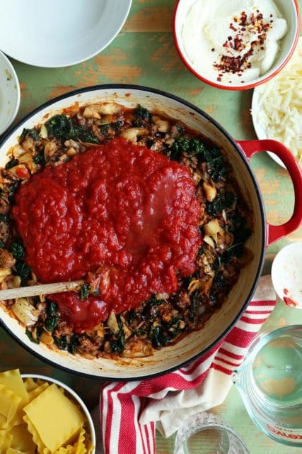 Tomato sauce added to sausage and kale for skillet lasagna