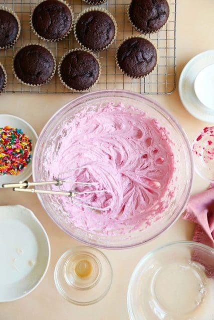 Pink buttercream in a mixing bowl with beaters.