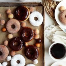 Glazed and sugared doughnuts on a baking sheet with hot coffee.