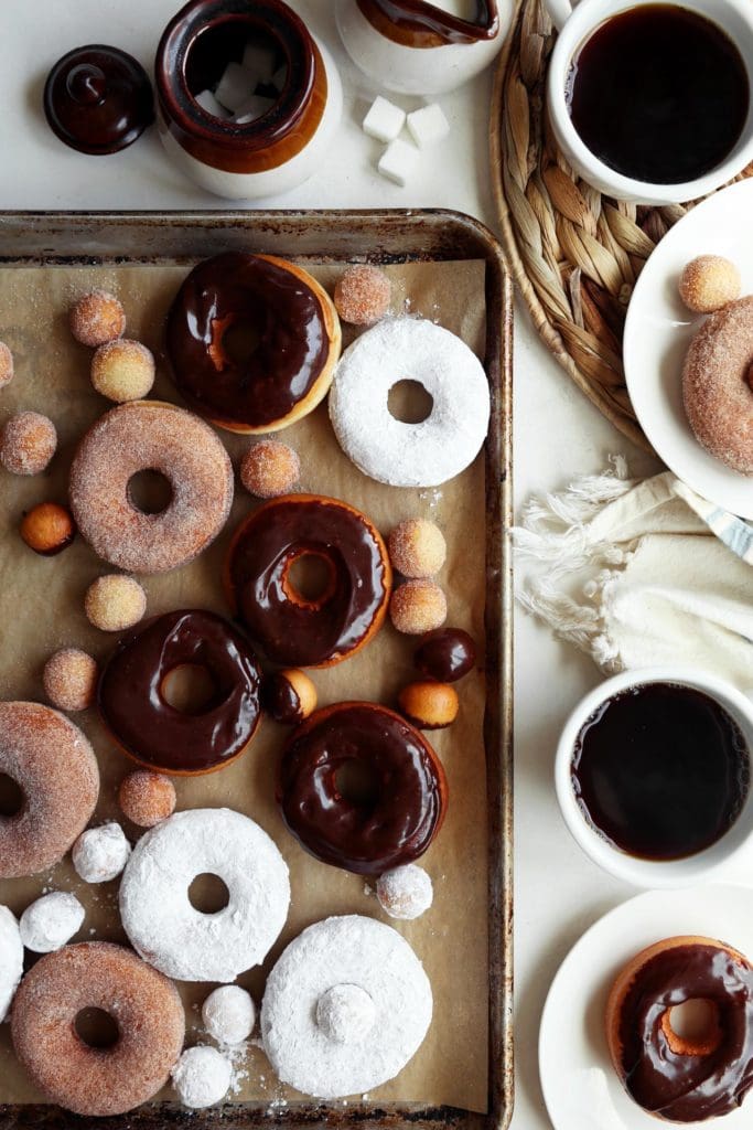 Glazed and sugared doughnuts on a baking sheet with hot coffee. 