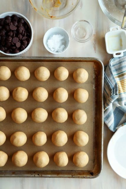 Rolled peanut butter balls on a parchment lined sheet.