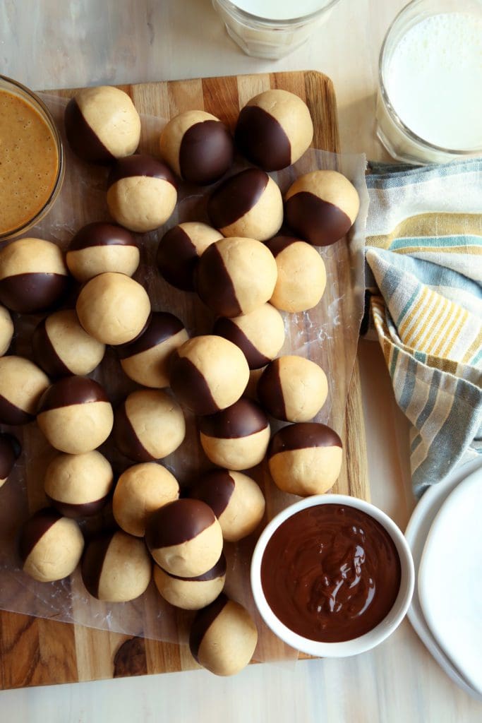 Peanut butter balls piled onto a wooden board with melted chocolate.