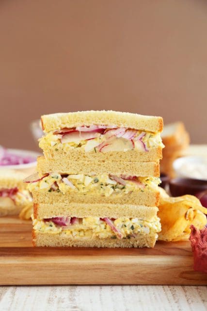 Two egg salad sandwiches sliced in half and stacked.