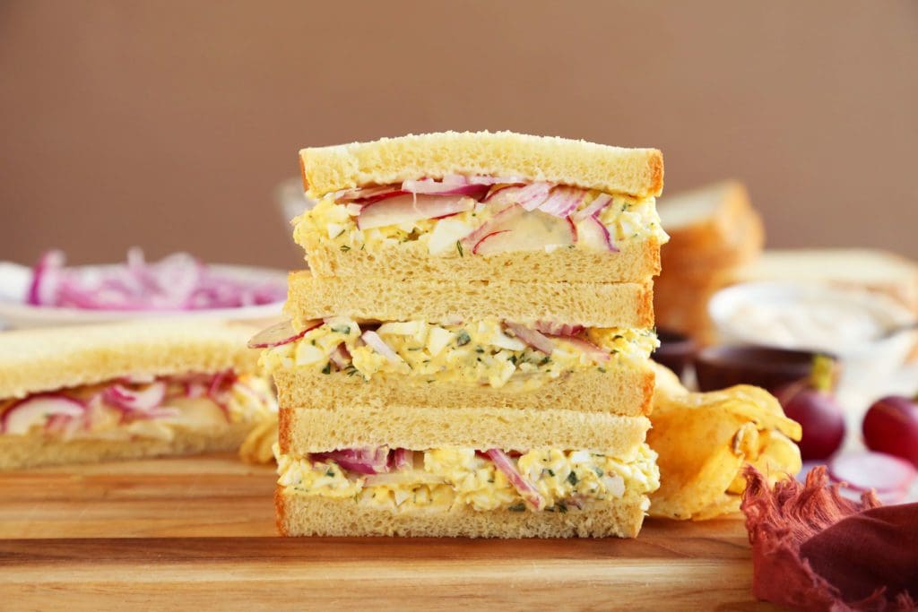 Two egg salad sandwiches sliced in half and stacked.