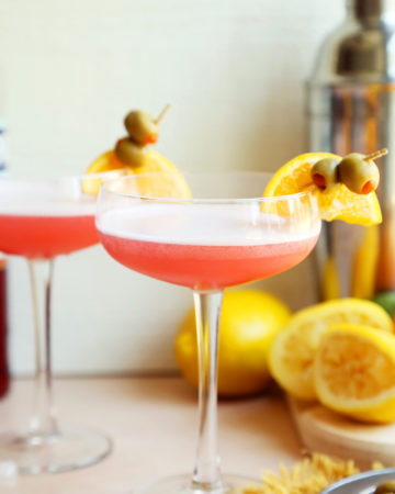 Gin sour cocktails in tall classes garnished with olives and orange slices.