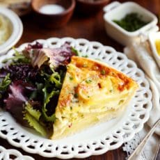 A slice of potato leek quiche on a white plate with salad.