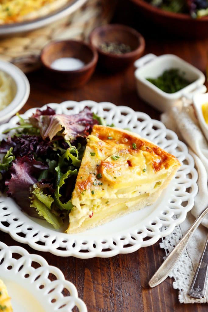 A slice of potato leek quiche on a white plate with salad.
