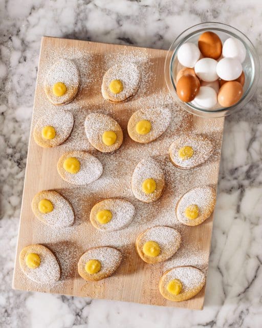 Lemon curd sandwich cookies on a board with dusting powdered sugar.