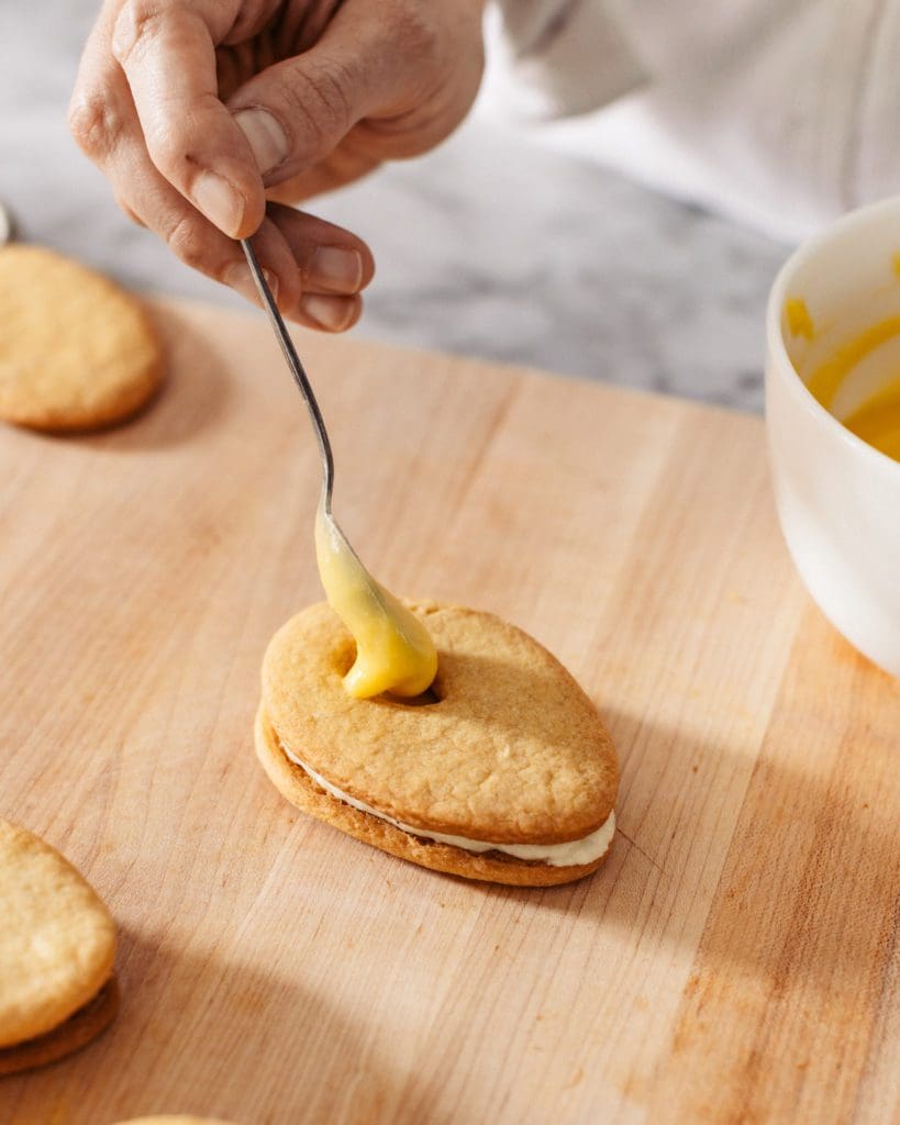 Spooning lemon curd onto lemon cookie.