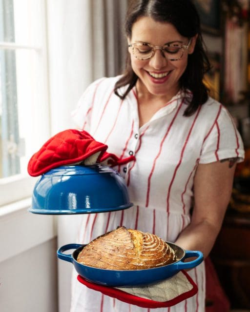 joy holding a hot pan of no-knead bread in bread oven.