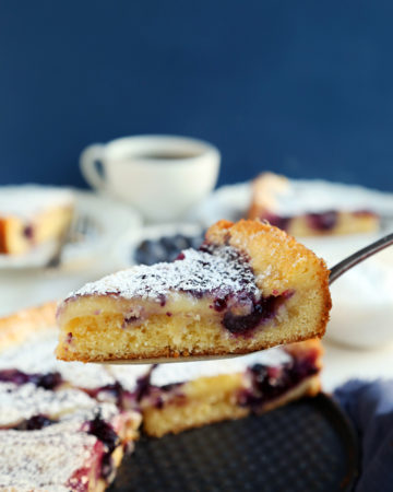 A slice of lemon blueberry gooey butter cake held on a cake slicer.