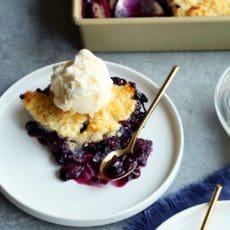 fresh baked blueberry cobbler on a plate with vanilla ice cream on top.
