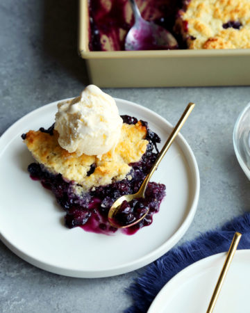 fresh baked blueberry cobbler on a plate with vanilla ice cream on top.