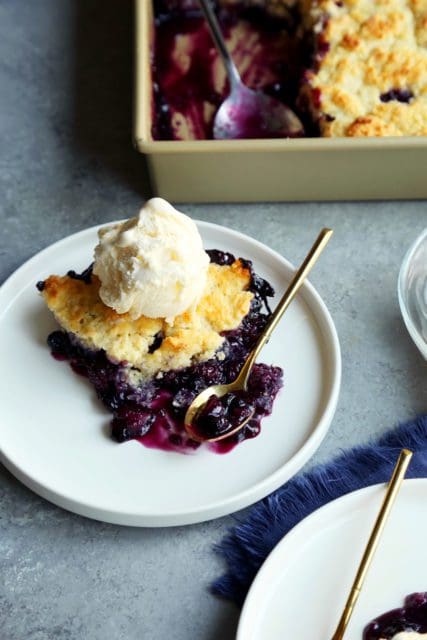 fresh baked blueberry cobbler on a plate with vanilla ice cream on top.