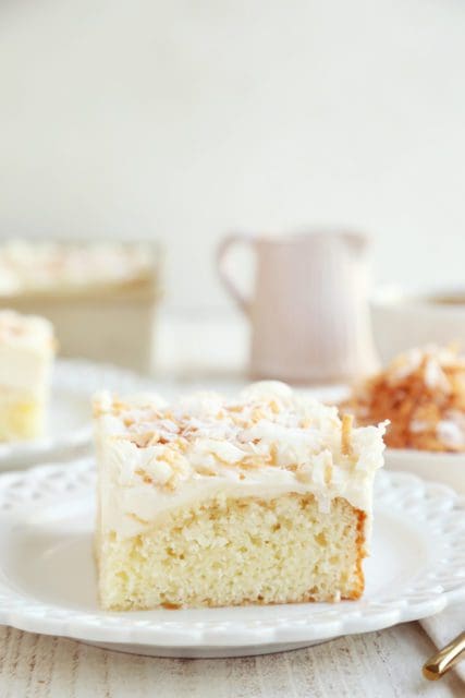 Slice of coconut cake on small white plate with coffee.