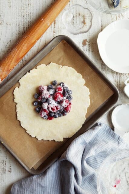 Rolled out pie crust with berries in center on small baking sheet.