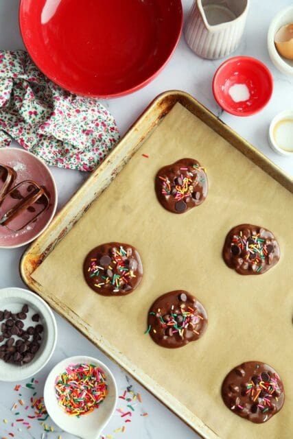 Brownie cookie batter on parchment lined baking sheet with sprinkles and chips