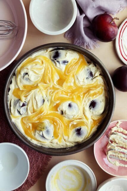Plum cake recipe in baking pan swirled with lemon curd.