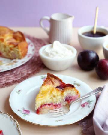 Slice of fresh plum cake recipe on small plate with fork