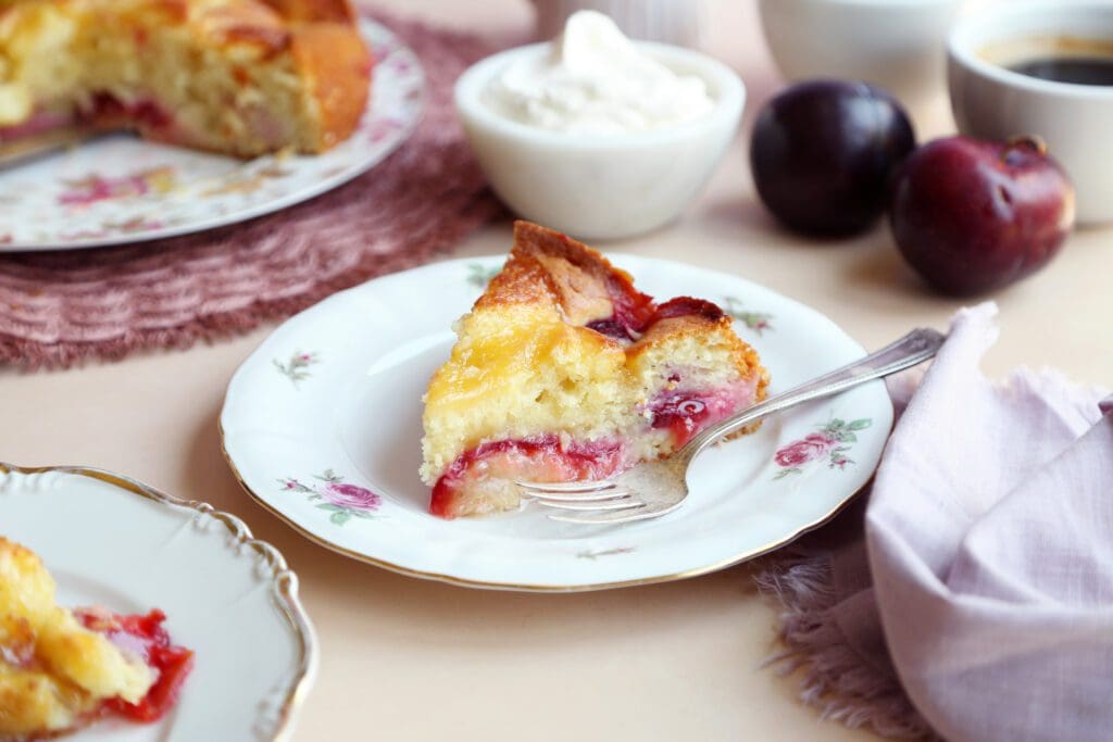 Slice of fresh plum cake on small plate with fork