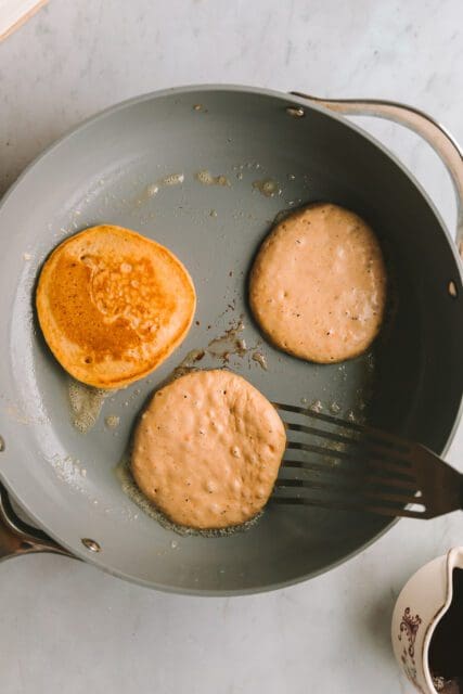 three small pancakes cooking in a skillets
