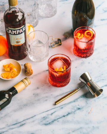 Two glasses of Negroni Sbagliato on a marble countertop.