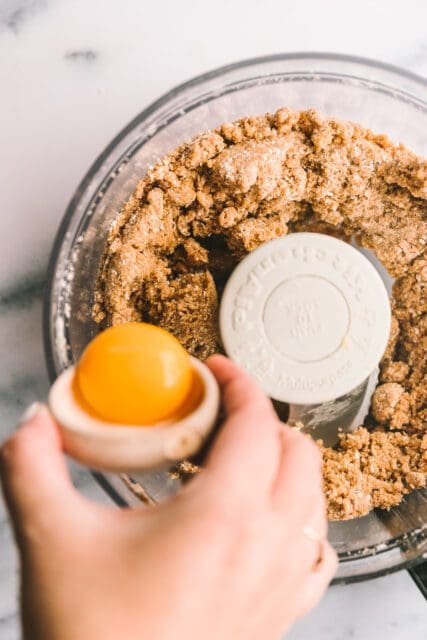 Adding egg yolk to cookie batter in food processor.
