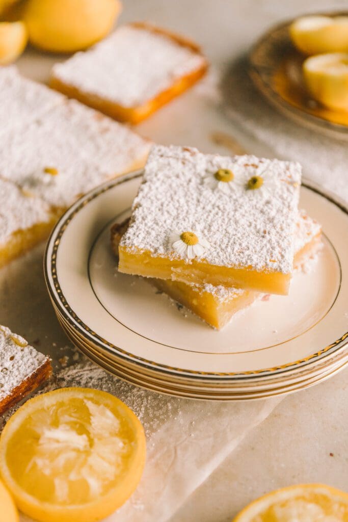 two lemon bars stacked on top of each other on a plate surrounded by other lemon bars
