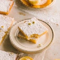 wider shot of lemon bars stacked on a plate with a bite taken out of one lemon bar