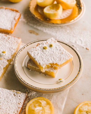 wider shot of lemon bars stacked on a plate with a bite taken out of one lemon bar