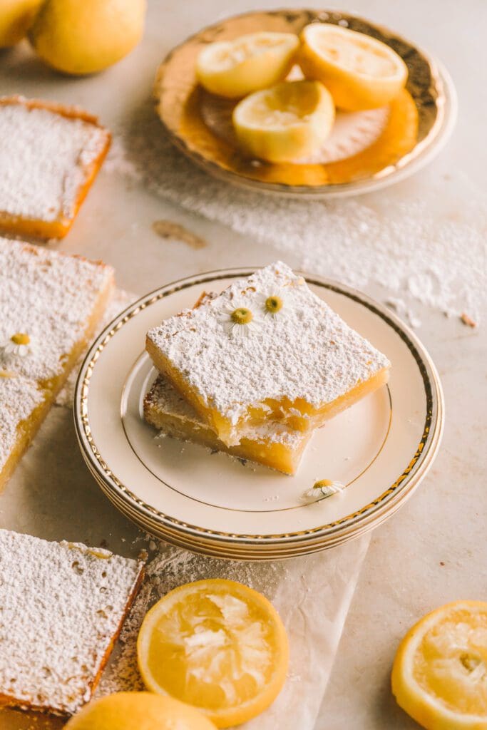 wider shot of lemon bars stacked on a plate with a bite taken out of one lemon bar
