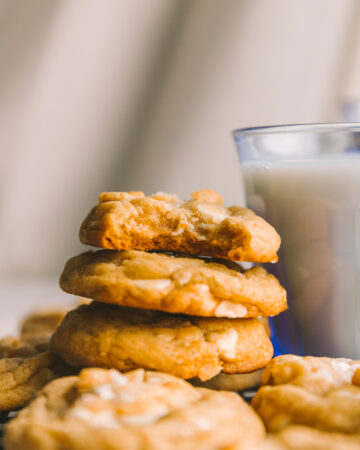 a stack of white chocolate macadamia nut cookies with a bite taken out of the top one with milk