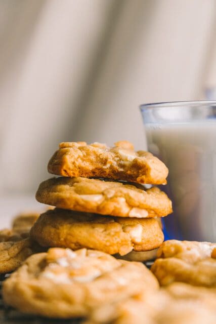 a stack of white chocolate macadamia nut cookies with a bite taken out of the top one with milk