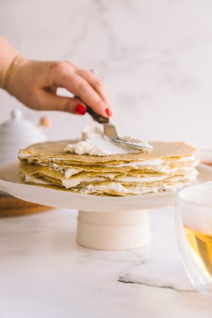 spreading soft whipped cream on layers of crepes