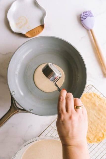 pouring crepe batter into a hot pan to make crepe cake