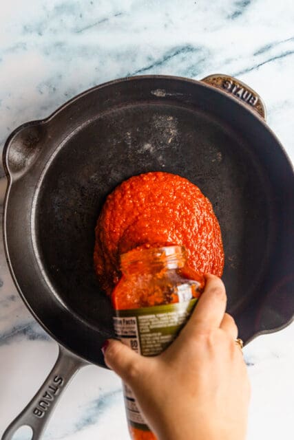 pouring tomato sauce into a cast iron pan