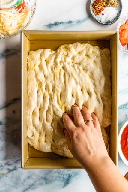 pressing dough into a pan, gently dimpling it with your fingers, for focaccia pizza