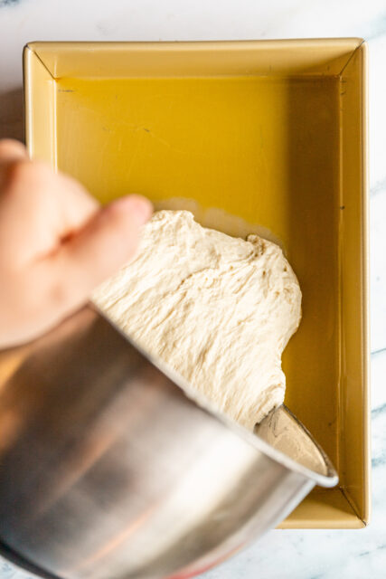 transferring focaccia dough from its bowl to a pan to bake
