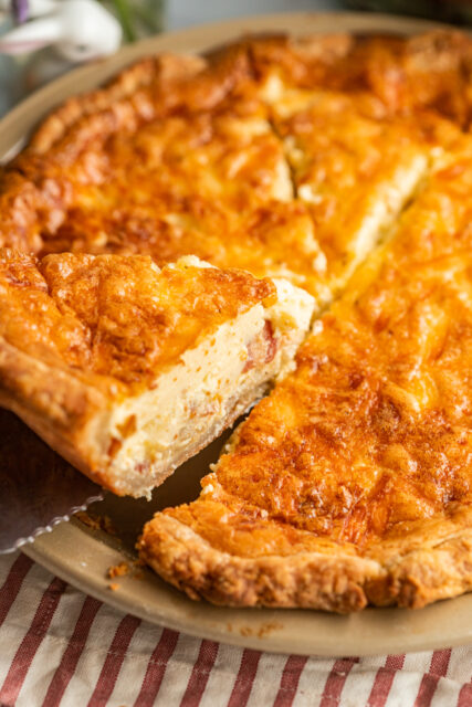 a slice of quiche Lorraine, showing off it's cheese, bacon, eggs, and onion insides